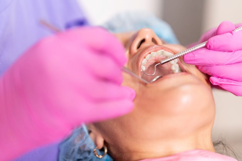 Dentist with pink gloves examining the patient’s teeth using dental tools during a procedure.