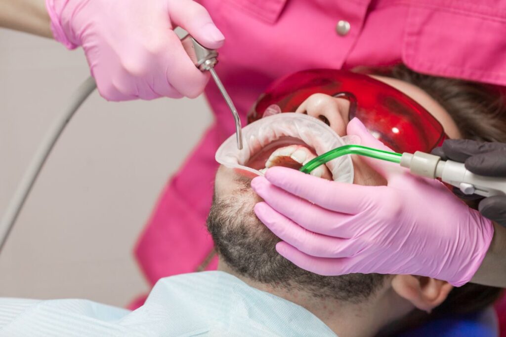 Dentist with pink gloves using dental instruments and suction in a patient’s open mouth