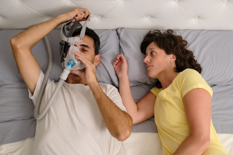 Man adjusting a CPAP mask beside his partner